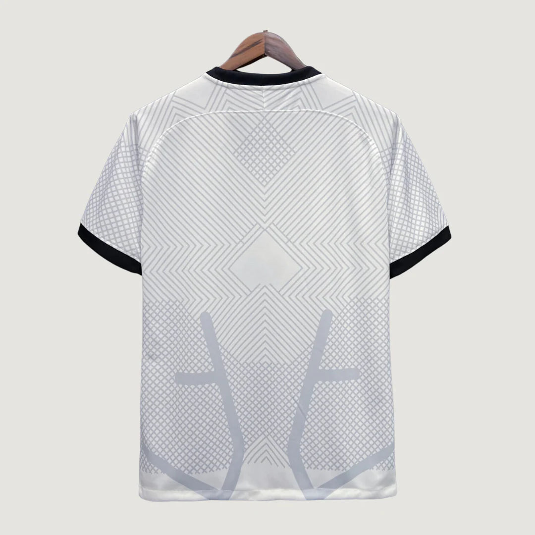 Dos d'un maillot de foot blanc avec motifs géométriques gris et manches à liseré noir.