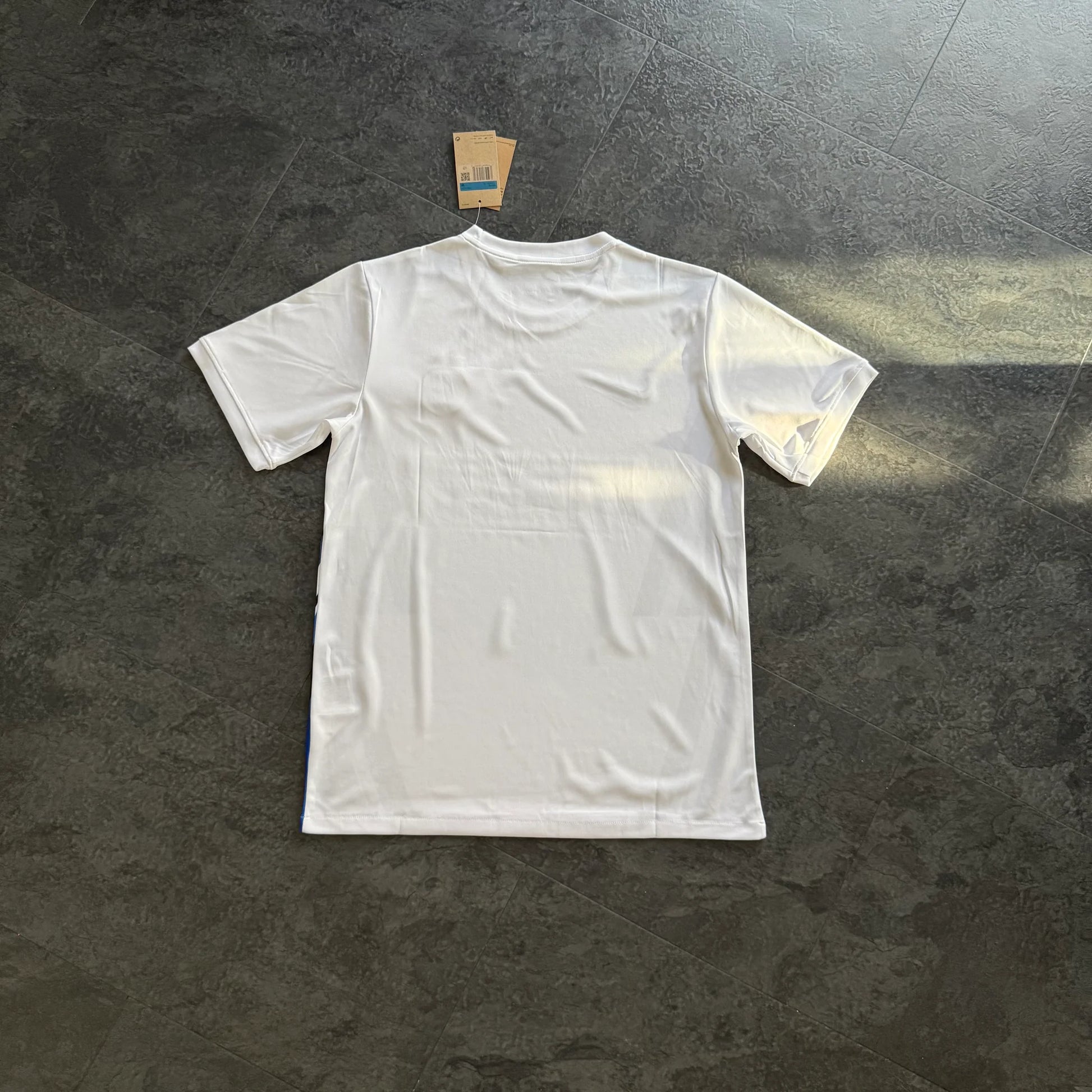 Maillot de foot blanc uni vu de dos, posé au sol, étiquette visible